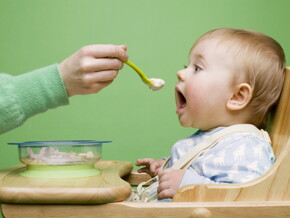 Bebé de un año sentado en una periquera a punto de comer de una cuchara Bebé de un año sentado en una periquera a punto de comer de una cuchara