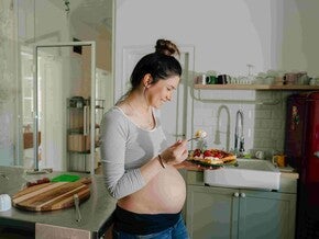 Mujer embarazada sonriendo en la cocina comiendo antojo dulce
