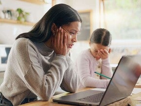 Madre y niña sentadas en la mesa de la cocina con una computadora portátil, realizando una actividad escolar en casa.
