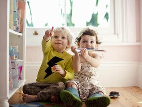 Niño y niña de dos años sentados en el piso, señalando. Concepto de comunicación y desarrollo de lenguaje.