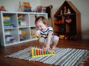 Niña de dos años jugando sobre la alfombra con ábaco de madera. Juego tranquilo como rutina diaria.