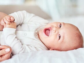 Conoce 3 tips para quitar el hipo al bebé fácilmente Bebé acostado en una cama riendo y jugando.