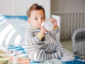 Niño pequeño sentado, tomando leche Nido en un vaso entrenador.