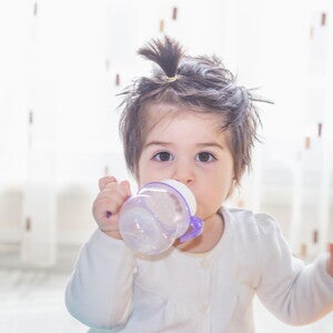 Niña pequeña tomando leche de crecimiento Nido en un vaso entrenador.