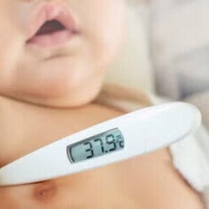 Cómo bajar la fiebre en bebés Bebé con fiebre, con un termómetro digital en su axila.