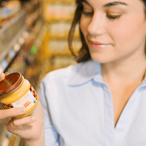Aprende a leer las etiquetas nutricionales Mujer leyendo etiqueta nutricional con un frasco de colado para bebes