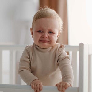 Bebé pequeño llorando dentro de su cuna, con expresión de incomodidad. 