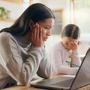 Madre y niña sentadas en la mesa de la cocina con una computadora portátil, realizando una actividad escolar en casa.