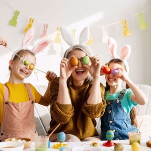 Padres y niños celebrando Pascua, cubriendo sus ojos con huevos de colores de forma divertida.