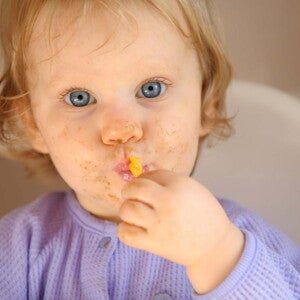 Bebé con restos de comida en la cara comiendo con una cuchara en su silla de alimentación