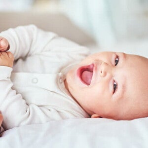 Conoce 3 tips para quitar el hipo al bebé fácilmente Bebé acostado en una cama riendo y jugando.
