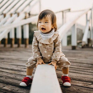 Conoce qué es el desarrollo psicomotor en los niños y bebés. Niña sorprendida sentada en un muro.