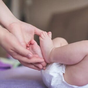 Cómo tratar las rozaduras de bebé en casa Mamá sosteniendo los pies de su bebé recién nacido en pañal.