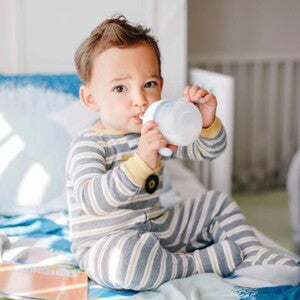 Niño pequeño sentado, tomando leche Nido en un vaso entrenador.
