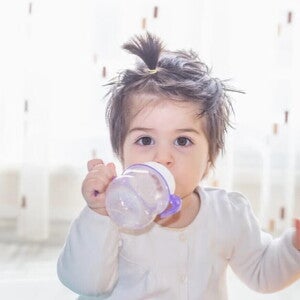 Niña pequeña tomando leche de crecimiento Nido en un vaso entrenador.