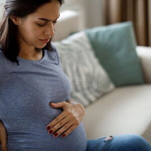 Conoce qué es la eclampsia en el embarazo y cuáles son sus causas. Mamá tocando el vientre y la espalda sintiendo molestia.