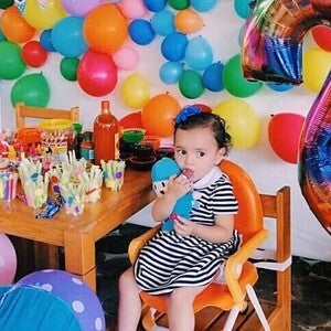 Pequeña sentada en una silla con globos a su alrededor disfrutando de Snacks para bebes