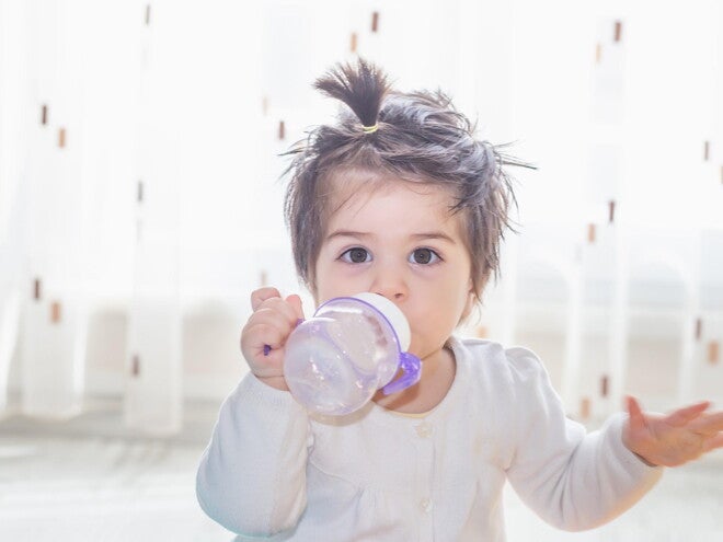 Niña pequeña tomando leche de crecimiento Nido en un vaso entrenador.