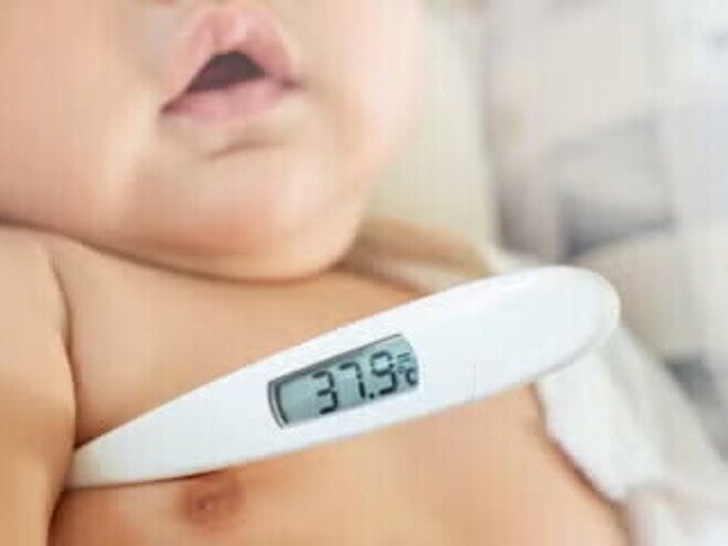 Cómo bajar la fiebre en bebés Bebé con fiebre, con un termómetro digital en su axila.