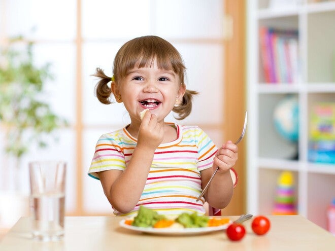 Pequeña comiendo verduras durante la comida.