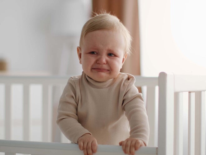 Bebé pequeño llorando dentro de su cuna, con expresión de incomodidad. 
