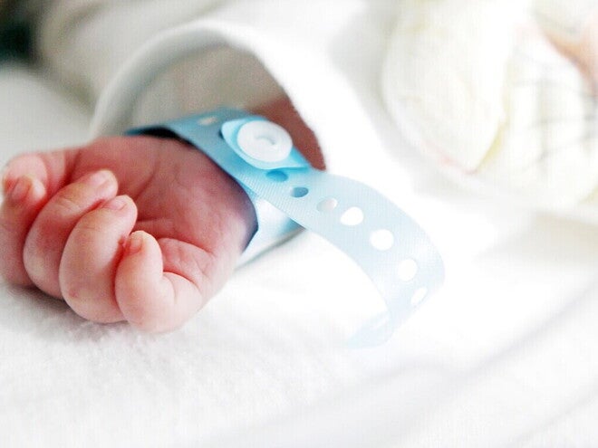 Mano de bebé recién nacido con pulsera de hospital. Pulsera indica peso del bebé al nacer