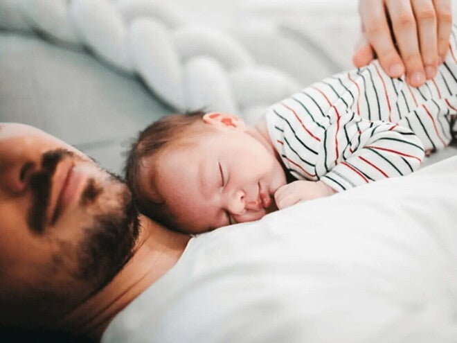 El significado de ser papá Bebé recostado encima de papá sobre la cama.