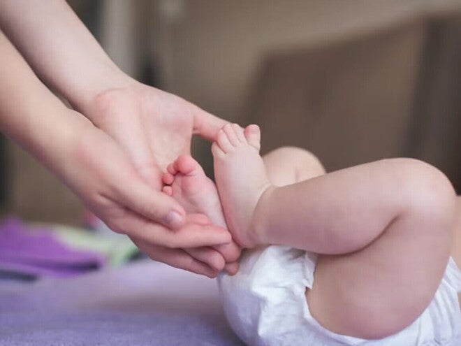 Mamá sosteniendo los pies de su bebé recién nacido en pañal.