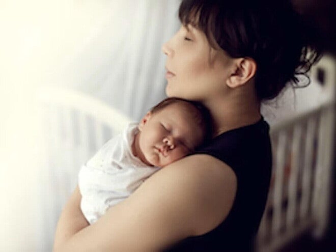 Mamá abrazando a bebé durmiendo en el periodo del puerperio. Cuidados para evitar complicaciones del puerperio
