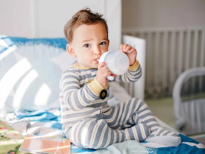 Niño pequeño sentado, tomando leche Nido en un vaso entrenador.