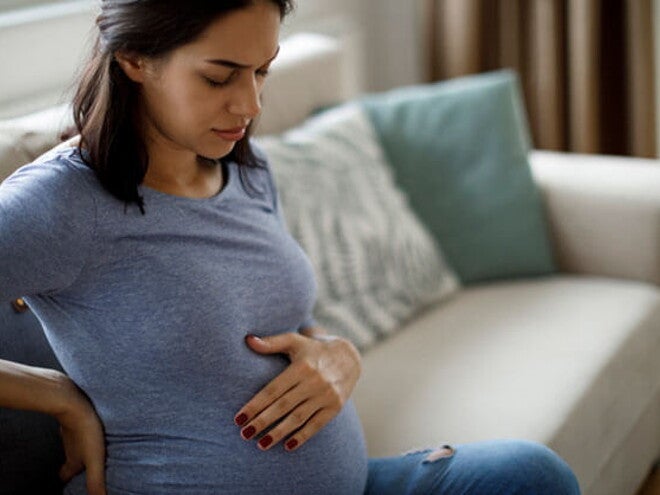 Conoce qué es la eclampsia en el embarazo y cuáles son sus causas. Mamá tocando el vientre y la espalda sintiendo molestia.