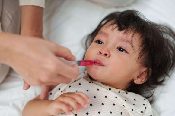 Persona adulta administrando medicamento líquido a un niño pequeño con una jeringa dosificadora.