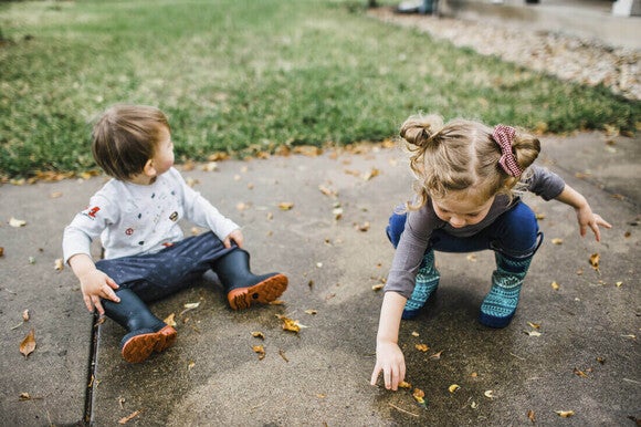 Niño y niña de dos años jugando afuera con hojas de la vereda, actividad para estimular el lenguaje