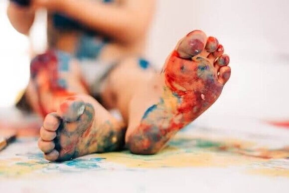 Arte que deja huella Niño con los pies pintados realizando dibujos sobre papel en el suelo.