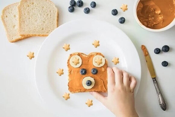 Sandwich con cara de osito Torta de crema de cacahuates, rodajas de plátano, arándanos y puffs Gerber formando la cara de un osito.