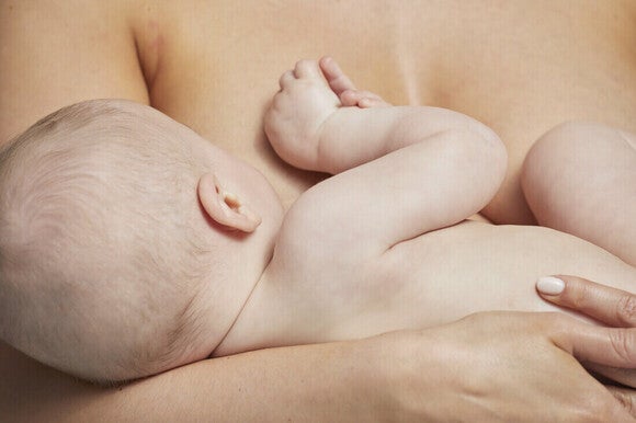 Mamá acostada dando de amamantar a su bebé, haciendo contacto piel con piel