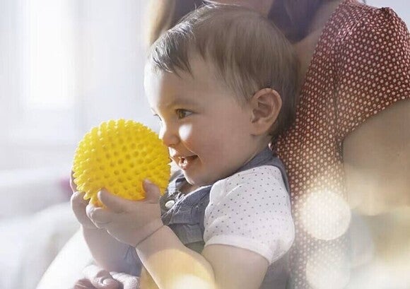 Bebé de 8 a 12 meses explorando una pelota sensorial de textura suave mientras desarrolla el agarre, la coordinación de las manos y la estimulación táctil mediante una actividad inspirada en el método Montessori.